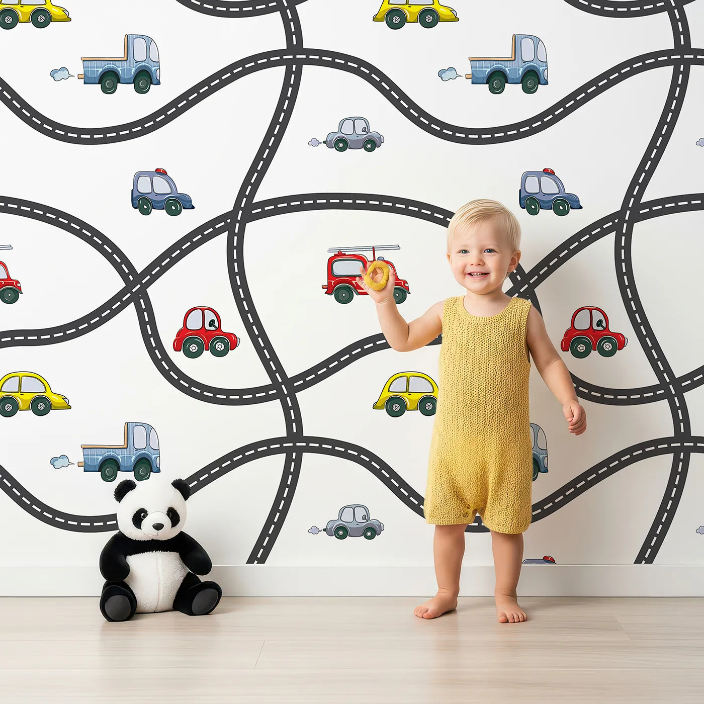 Lovely child standing in front of Whimsy Tots Bumper Buddies Road Maze Wallpaper in White with car, road, truck, taxi in design.