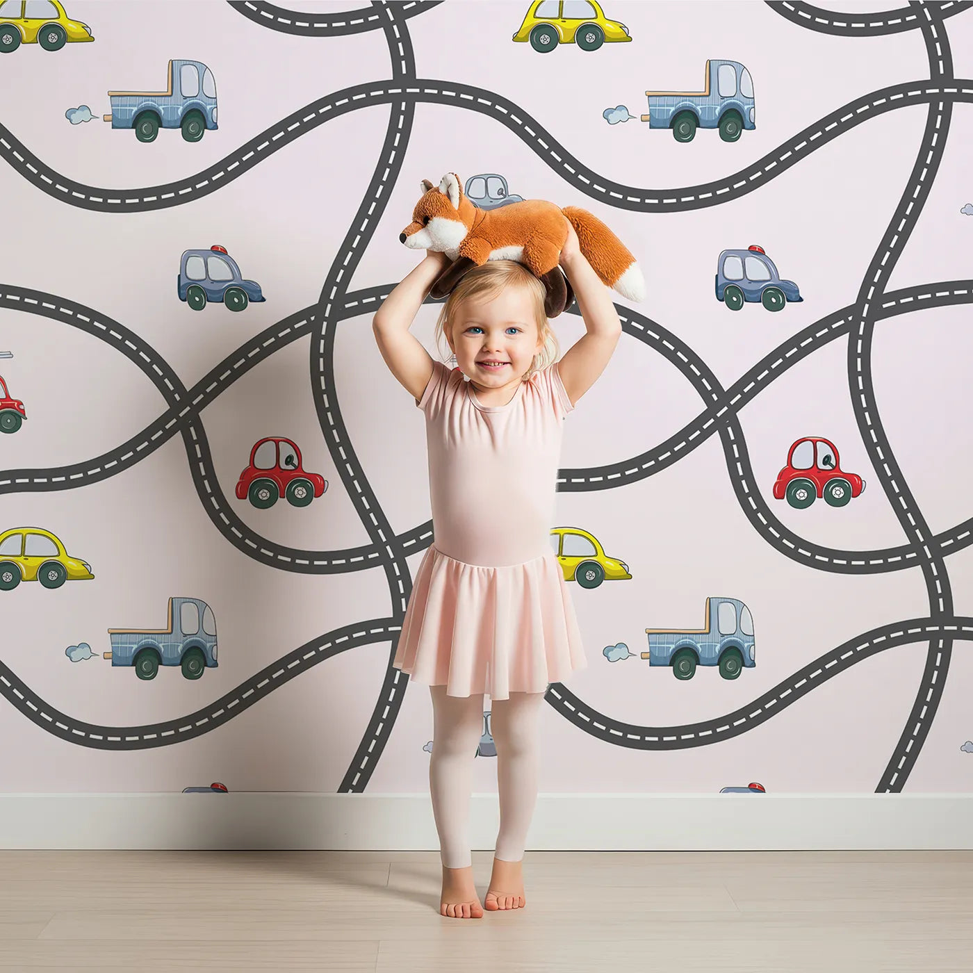 Lovely child standing in front of Whimsy Tots Bumper Buddies Road Maze Wallpaper in Soft Pink with car, road, truck, taxi in design.