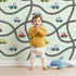 Lovely child standing in front of Whimsy Tots Bumper Buddies Road Maze Wallpaper in Mint Green with car, road, truck, taxi in design. Lovely child standing in front of Whimsy Tots Bumper Buddies Road Maze Wallpaper in Mint Green with car, road, truck, taxi in design.