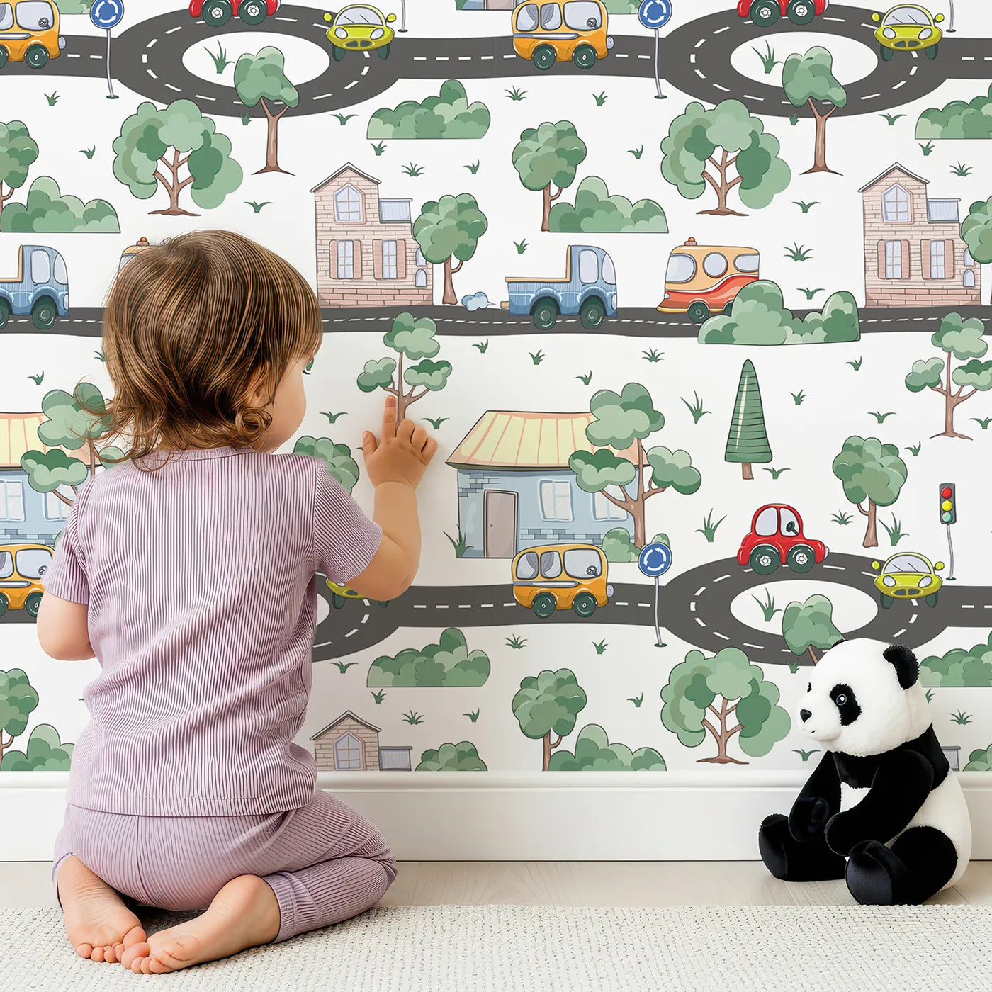 Lovely child standing in front of Whimsy Tots Bumper Buddies Town Tour Wallpaper in White with car, house, road, tree, stoplight in design.