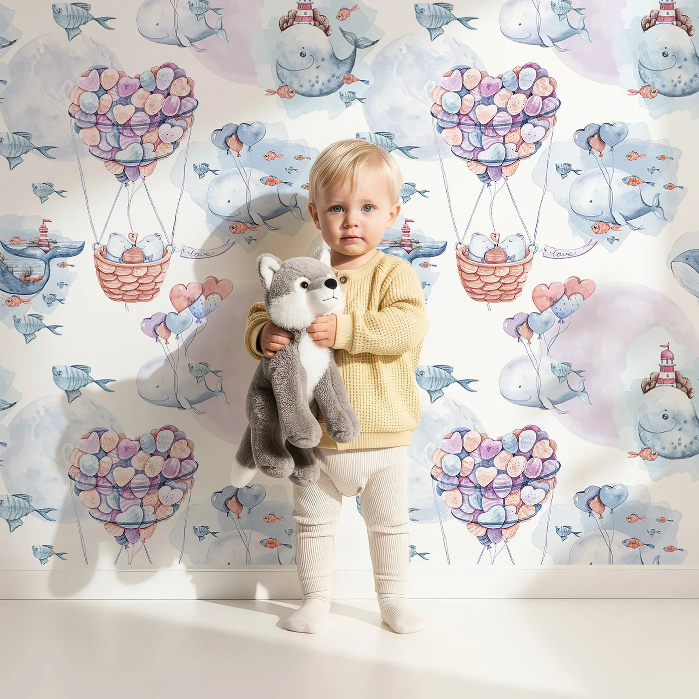 Lovely child standing in front of Whimsy Tots Whale Balloon Dreams Wallpaper with whale, balloon, fish, heart, lighthouse, bear in design.
