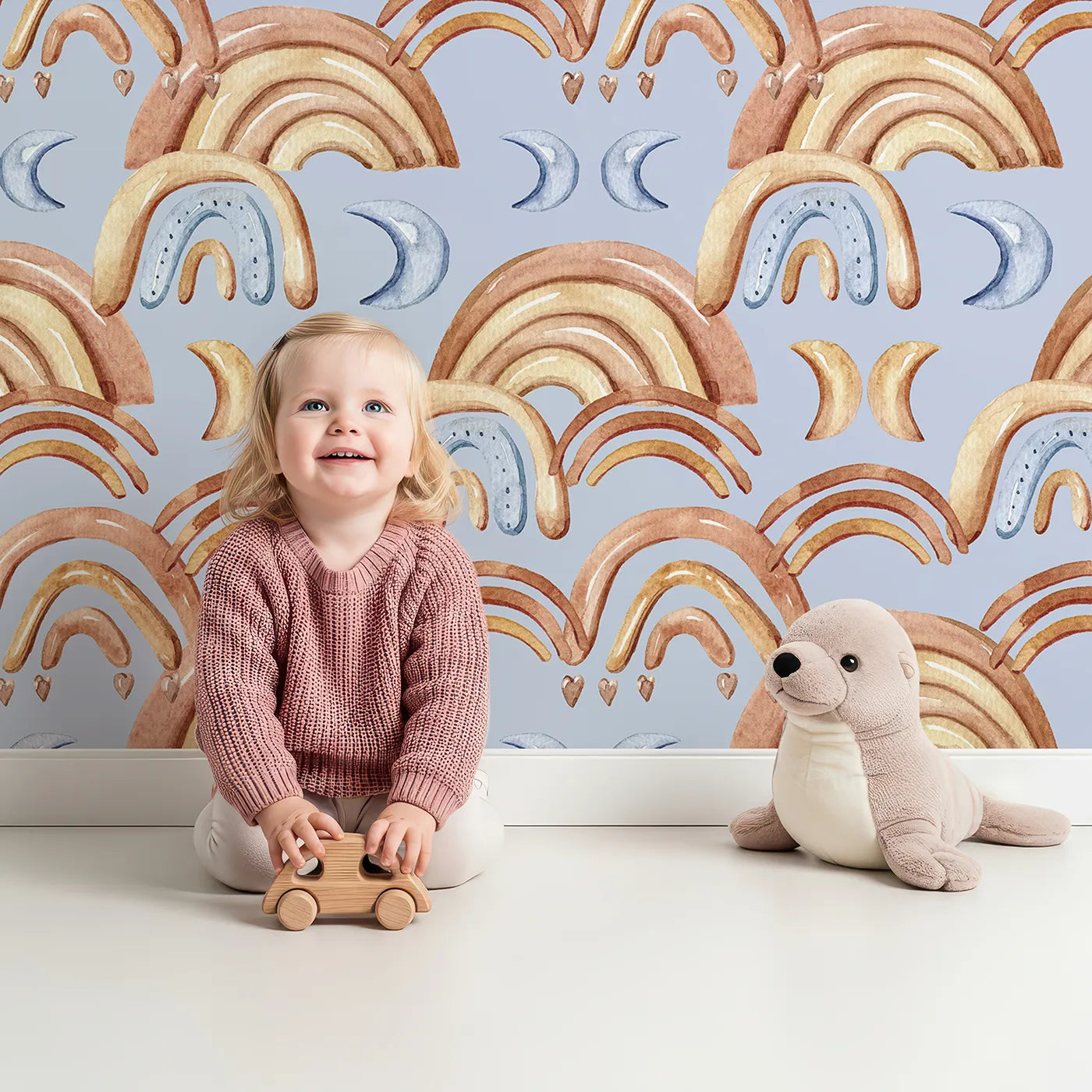 Lovely child standing in front of Whimsy Tots Rainbow Moondance Wallpaper in Blue with rainbow, moon, arc, heart in design.