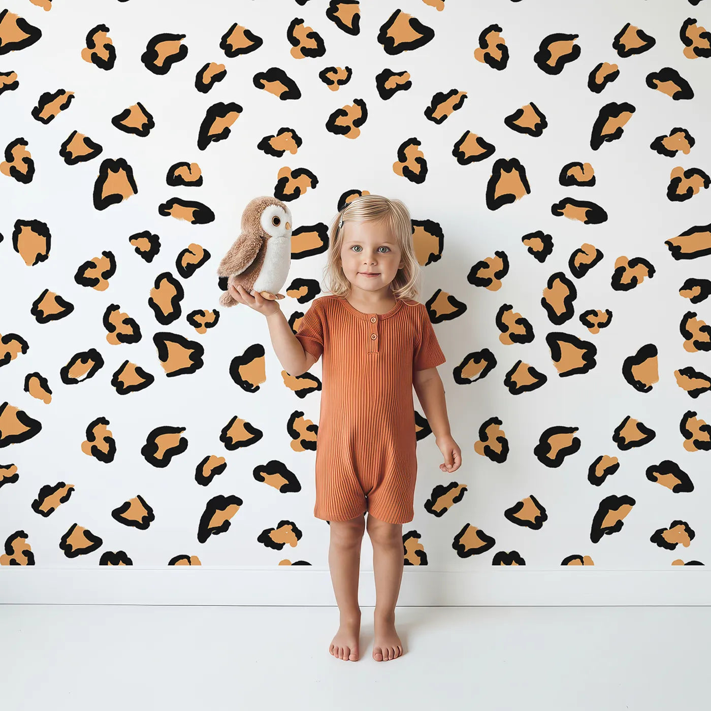 Lovely child standing in front of Whimsy Tots Playful Cub Spots Wallpaper in White with leopard, spot, pattern in design.