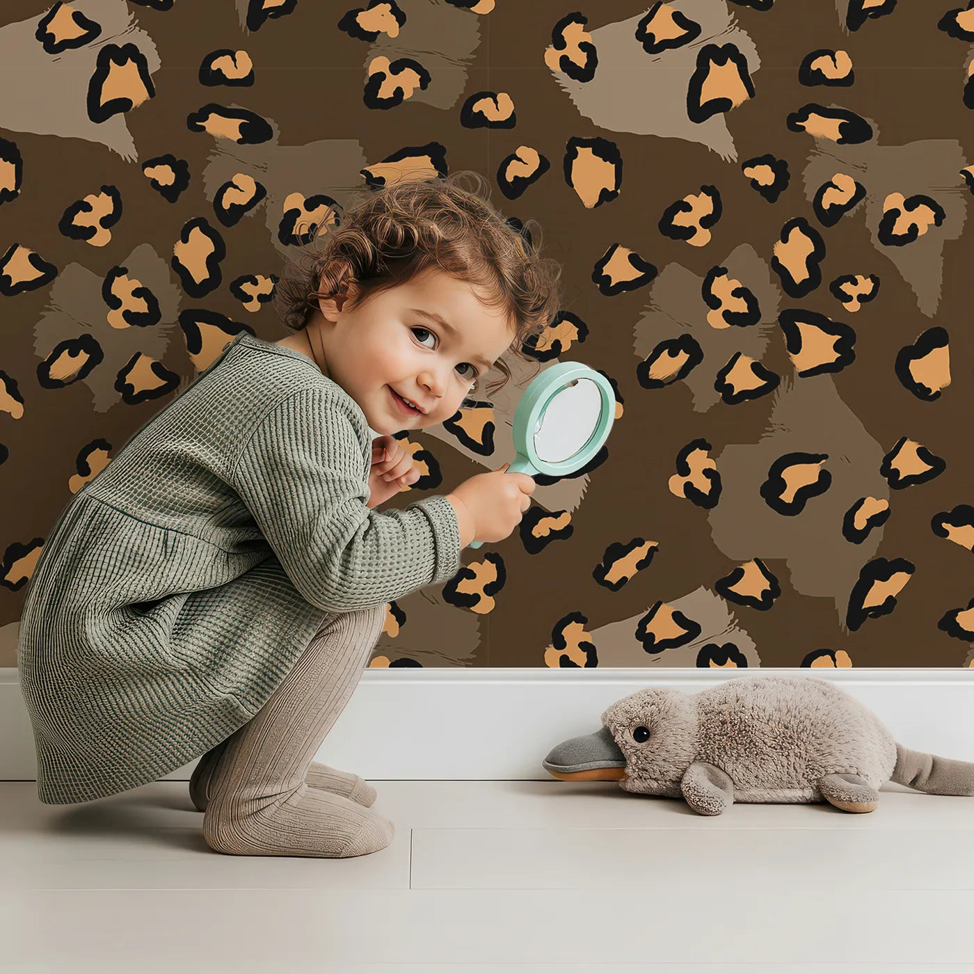 Lovely child standing in front of Whimsy Tots Playful Cub Spots Wallpaper in Brown with leopard, spot, pattern in design.