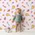 Lovely child standing in front of Whimsy Tots Autumn Forage Friends Wallpaper in Blush Pink with mushroom, acorn, cherry, pumpkin, heart in design. Lovely child standing in front of Whimsy Tots Autumn Forage Friends Wallpaper in Blush Pink with mushroom, acorn, cherry, pumpkin, heart in design.