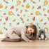 Lovely child standing in front of Whimsy Tots Autumn Forage Friends Wallpaper in Green with mushroom, acorn, cherry, pumpkin, heart in design. Lovely child standing in front of Whimsy Tots Autumn Forage Friends Wallpaper in Green with mushroom, acorn, cherry, pumpkin, heart in design.