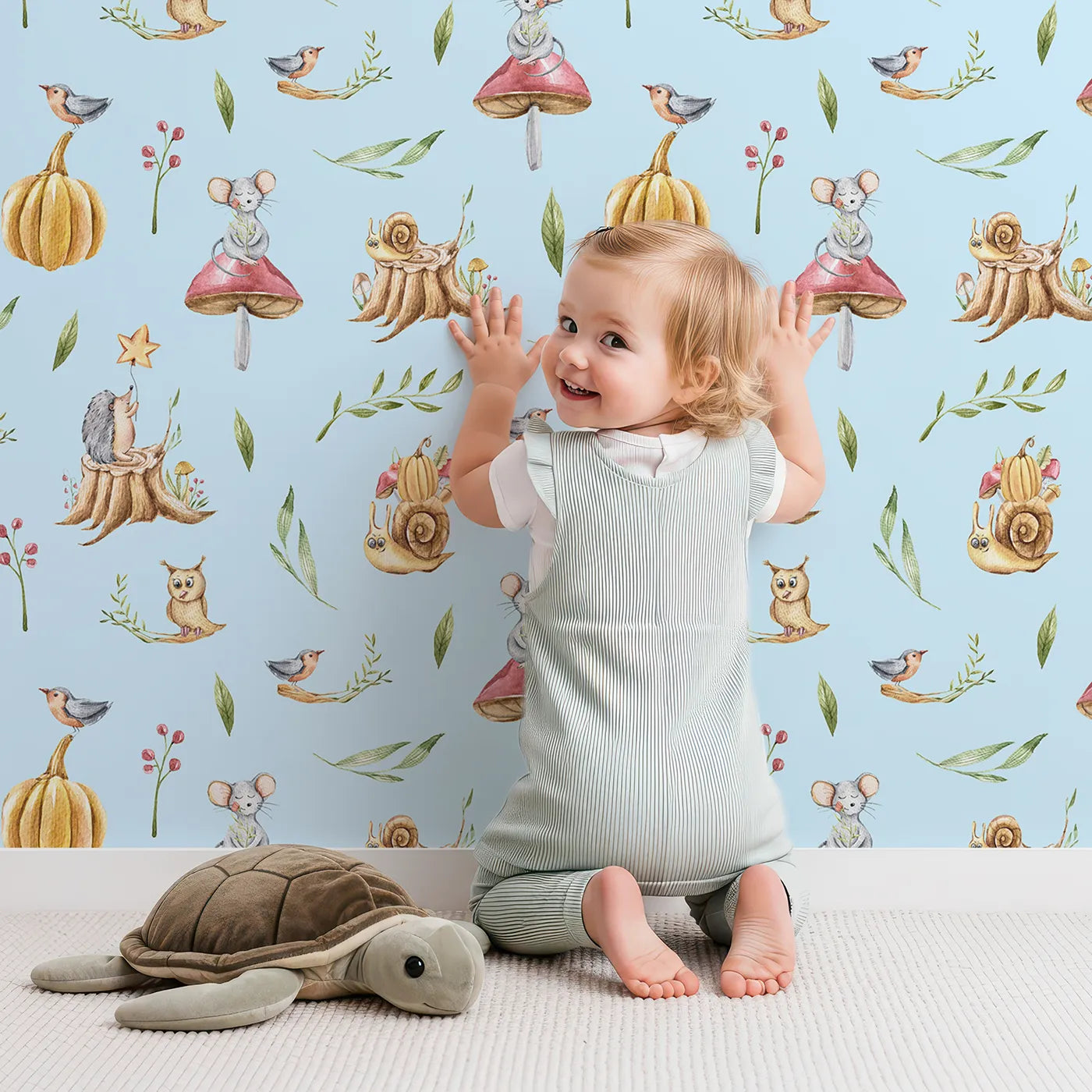 Lovely child standing in front of Whimsy Tots Wishful Woodland Friends Wallpaper in Sky Blue with hedgehog, owl, mouse, snail, mushroom, leaf, pumpkin, star in design.