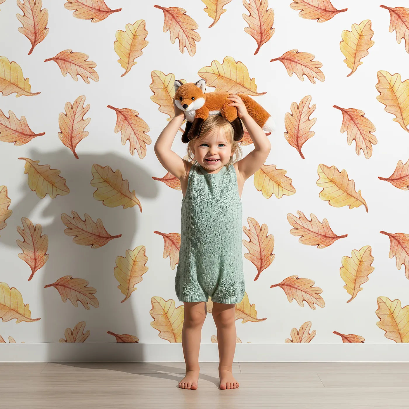 Lovely child standing in front of Whimsy Tots Falling Oak Whispers Wallpaper in White with oak leaf, leaf in design.