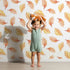 Lovely child standing in front of Whimsy Tots Falling Oak Whispers Wallpaper in White with oak leaf, leaf in design. Lovely child standing in front of Whimsy Tots Falling Oak Whispers Wallpaper in White with oak leaf, leaf in design.