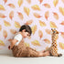 Lovely child standing in front of Whimsy Tots Falling Oak Whispers Wallpaper in Blush Pink with oak leaf, leaf in design. Lovely child standing in front of Whimsy Tots Falling Oak Whispers Wallpaper in Blush Pink with oak leaf, leaf in design.