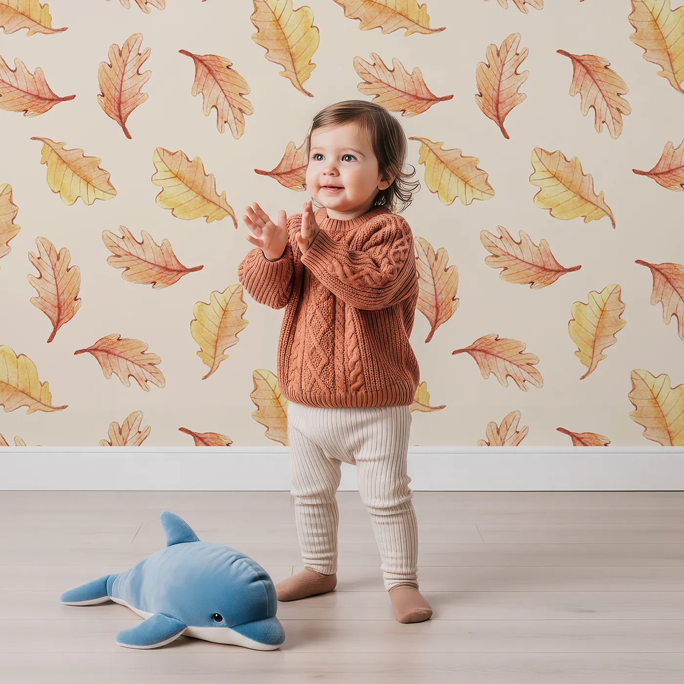 Lovely child standing in front of Whimsy Tots Falling Oak Whispers Wallpaper in Cream with oak leaf, leaf in design.