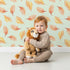 Lovely child standing in front of Whimsy Tots Falling Oak Whispers Wallpaper in Green with oak leaf, leaf in design. Lovely child standing in front of Whimsy Tots Falling Oak Whispers Wallpaper in Green with oak leaf, leaf in design.