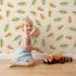 Lovely child standing in front of Whimsy Tots Acorn Meadow Whimsy Wallpaper in Cream with acorn, oak leaf, leaf in design. Lovely child standing in front of Whimsy Tots Acorn Meadow Whimsy Wallpaper in Cream with acorn, oak leaf, leaf in design.