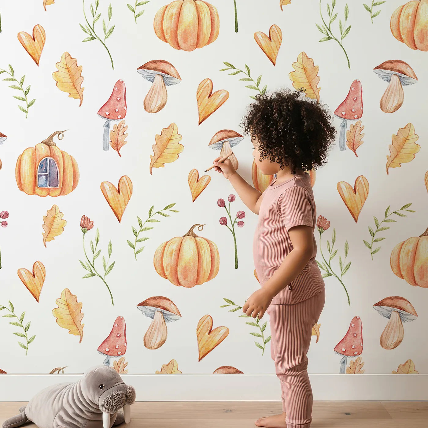 Lovely child standing in front of Whimsy Tots Pumpkin Heart Harvest Wallpaper in White with pumpkin, mushroom, leaf, heart, berry in design.