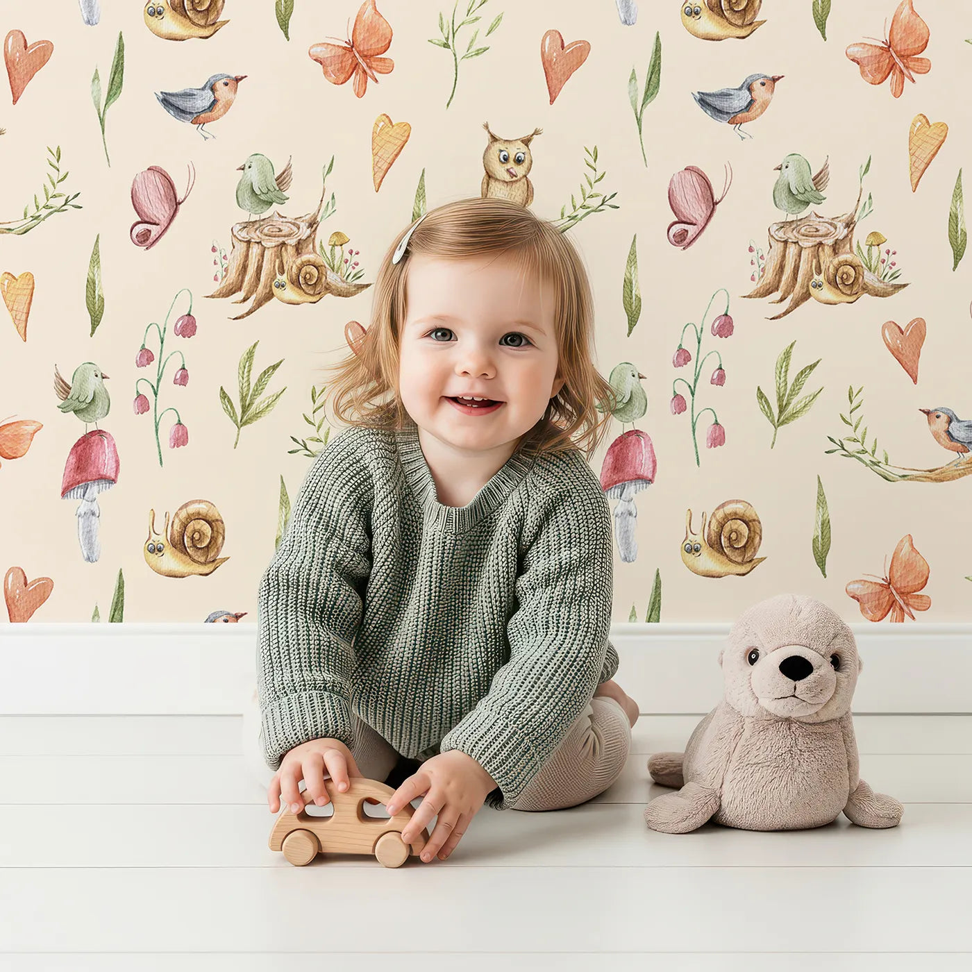 Lovely child standing in front of Whimsy Tots Woodland Playtime Parade Wallpaper in Cream with owl, bird, butterfly, snail, mushroom, heart, stump in design.