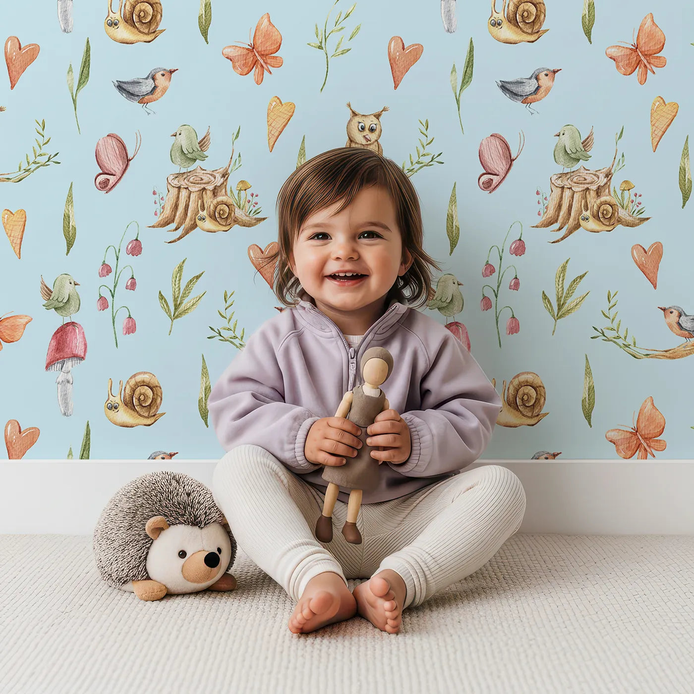 Lovely child standing in front of Whimsy Tots Woodland Playtime Parade Wallpaper in Sky with owl, bird, butterfly, snail, mushroom, heart, stump in design.