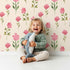 Lovely child standing in front of Whimsy Tots Pink Meadow Blossoms Wallpaper in Cream with flower, leaf in design. Lovely child standing in front of Whimsy Tots Pink Meadow Blossoms Wallpaper in Cream with flower, leaf in design.