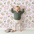 Lovely child standing in front of Whimsy Tots Botanical Berry Sprigs Wallpaper in Blush Pink with berry, leaf, sprig in design. Lovely child standing in front of Whimsy Tots Botanical Berry Sprigs Wallpaper in Blush Pink with berry, leaf, sprig in design.