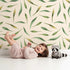 Lovely child standing in front of Whimsy Tots Whimsy Leaf Scatter Wallpaper in Cream with leaf, spray, greenery, foliage in design. Lovely child standing in front of Whimsy Tots Whimsy Leaf Scatter Wallpaper in Cream with leaf, spray, greenery, foliage in design.