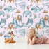 Lovely child standing in front of Whimsy Tots Whale Balloon Parade Wallpaper in Blush Pink with whale, balloon, octopus, bunting, seaweed, crown in design. Lovely child standing in front of Whimsy Tots Whale Balloon Parade Wallpaper in Blush Pink with whale, balloon, octopus, bunting, seaweed, crown in design.