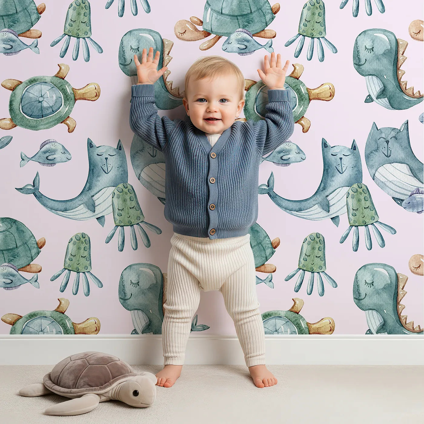 Lovely child standing in front of Whimsy Tots Ocean Daydream Creatures Wallpaper in Blush Pink with whale, fish, turtle, octopus, dinosaur, seaweed in design.