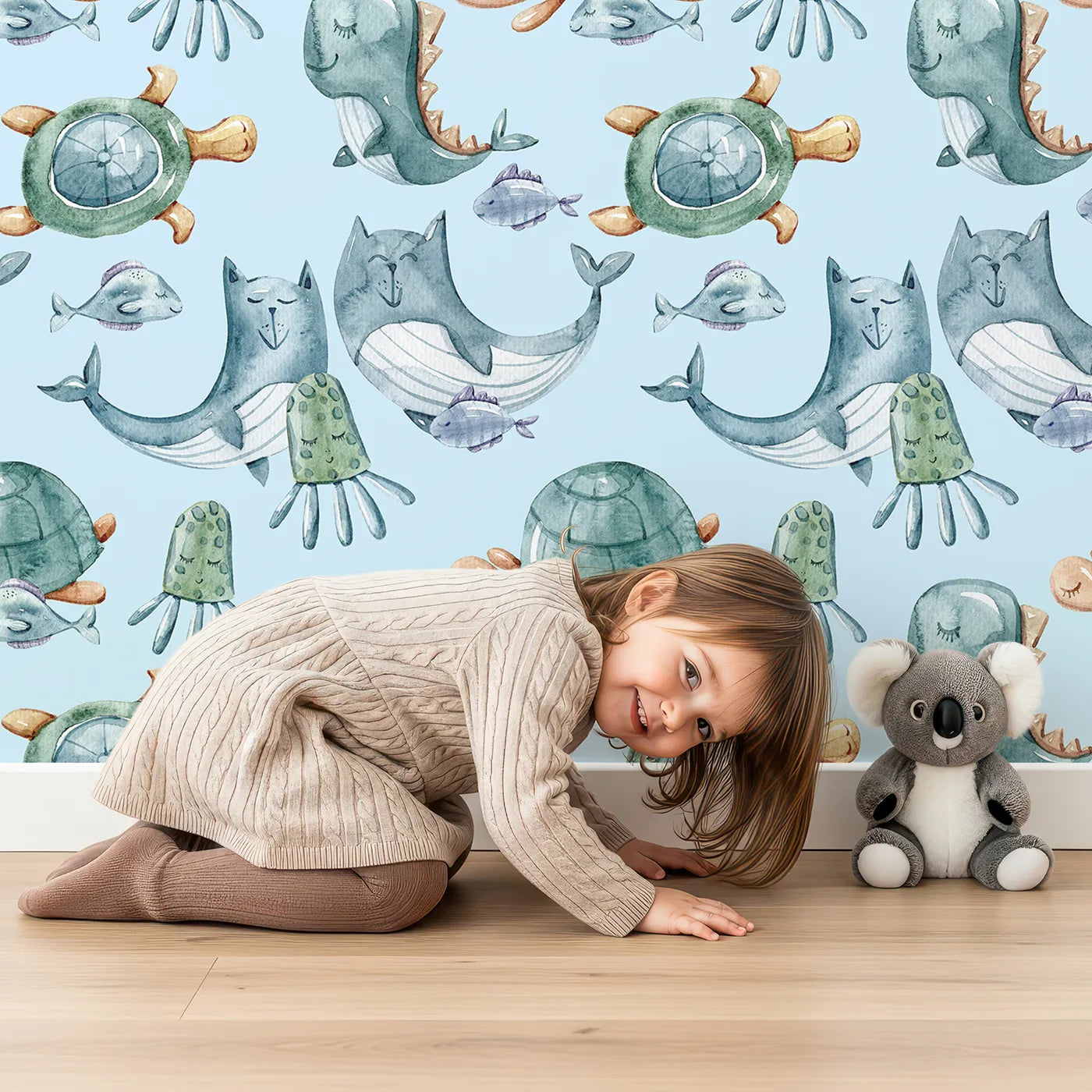 Lovely child standing in front of Whimsy Tots Ocean Daydream Creatures Wallpaper in Sky Blue with whale, fish, turtle, octopus, dinosaur, seaweed in design.