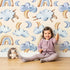 Lovely child standing in front of Whimsy Tots Sleepy Skies Wallpaper in Cream with cloud, moon, rainbow, sheep in design. Lovely child standing in front of Whimsy Tots Sleepy Skies Wallpaper in Cream with cloud, moon, rainbow, sheep in design.