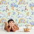 Lovely child standing in front of Whimsy Tots Sleepy Skies Wallpaper in Mint Green with cloud, moon, rainbow, sheep in design. Lovely child standing in front of Whimsy Tots Sleepy Skies Wallpaper in Mint Green with cloud, moon, rainbow, sheep in design.