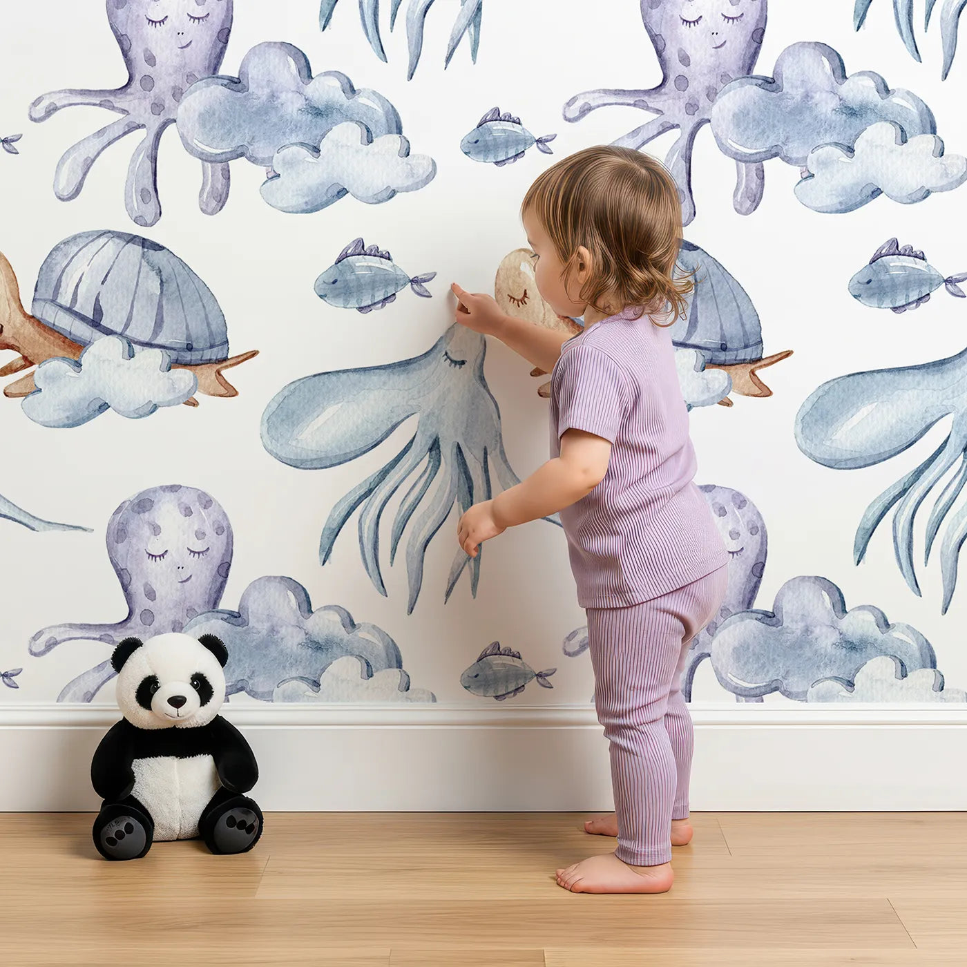 Lovely child standing in front of Whimsy Tots Ocean Dreams Wallpaper in White with cloud, turtle, octopus, squid, fish in design.