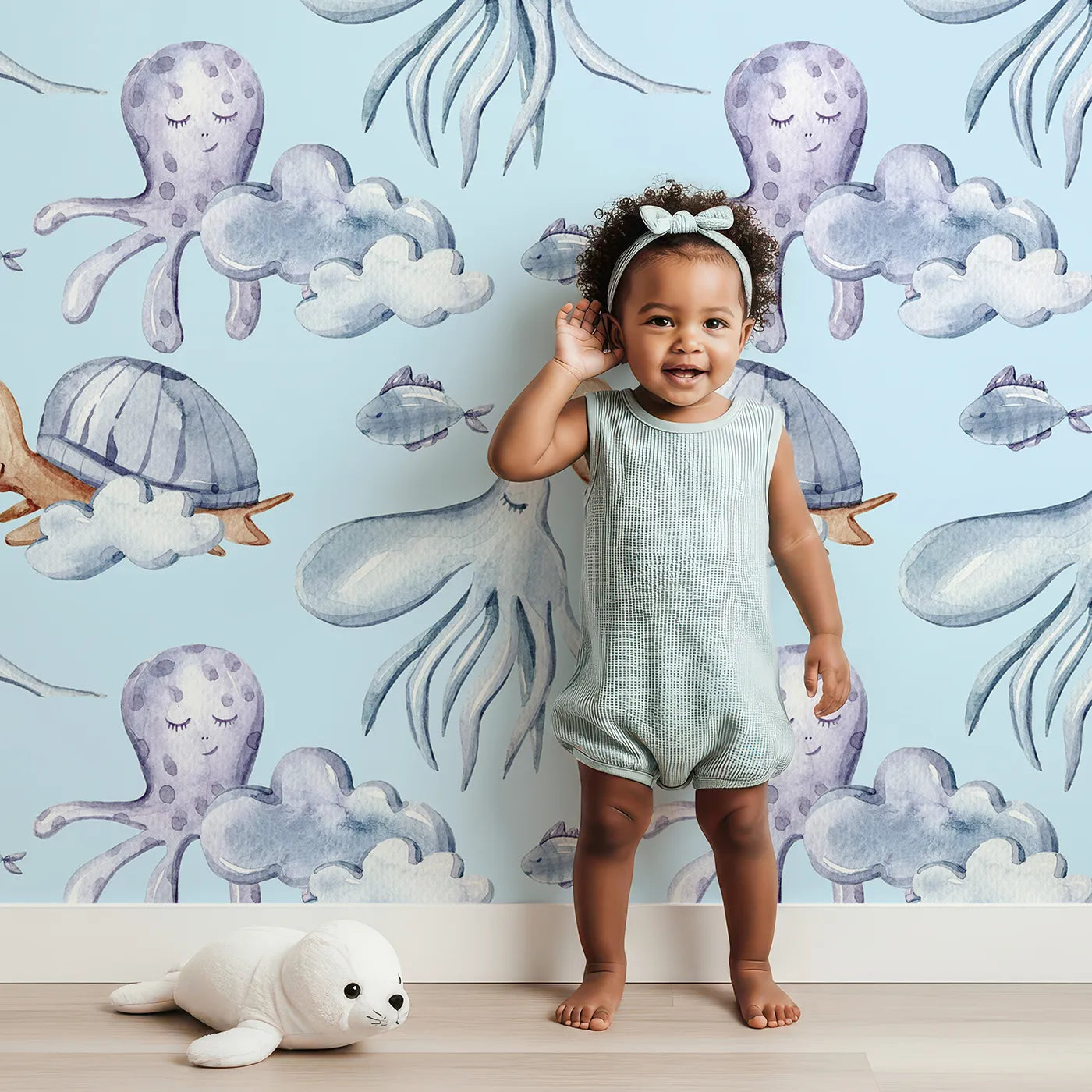 Lovely child standing in front of Whimsy Tots Ocean Dreams Wallpaper in Blue with cloud, turtle, octopus, squid, fish in design.