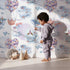 Lovely child standing in front of Whimsy Tots Whales of Love Wallpaper in White with whale, balloon, heart, lighthouse, fish in design. Lovely child standing in front of Whimsy Tots Whales of Love Wallpaper in White with whale, balloon, heart, lighthouse, fish in design.