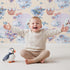Lovely child standing in front of Whimsy Tots Whales of Love Wallpaper in Cream with whale, balloon, heart, lighthouse, bear, fish in design. Lovely child standing in front of Whimsy Tots Whales of Love Wallpaper in Cream with whale, balloon, heart, lighthouse, bear, fish in design.