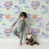 Lovely child standing in front of Whimsy Tots Whales of Love Wallpaper in Mint Green with whale, balloon, heart, lighthouse, bear, fish in design. Lovely child standing in front of Whimsy Tots Whales of Love Wallpaper in Mint Green with whale, balloon, heart, lighthouse, bear, fish in design.