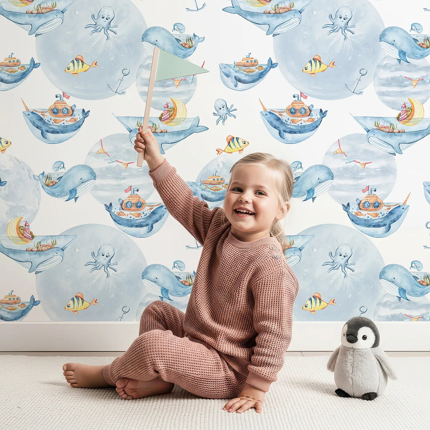 Lovely child standing in front of Whimsy Tots Whale Boat Parade Wallpaper in White with whale, submarine, boat, octopus, anchor, flag in design.