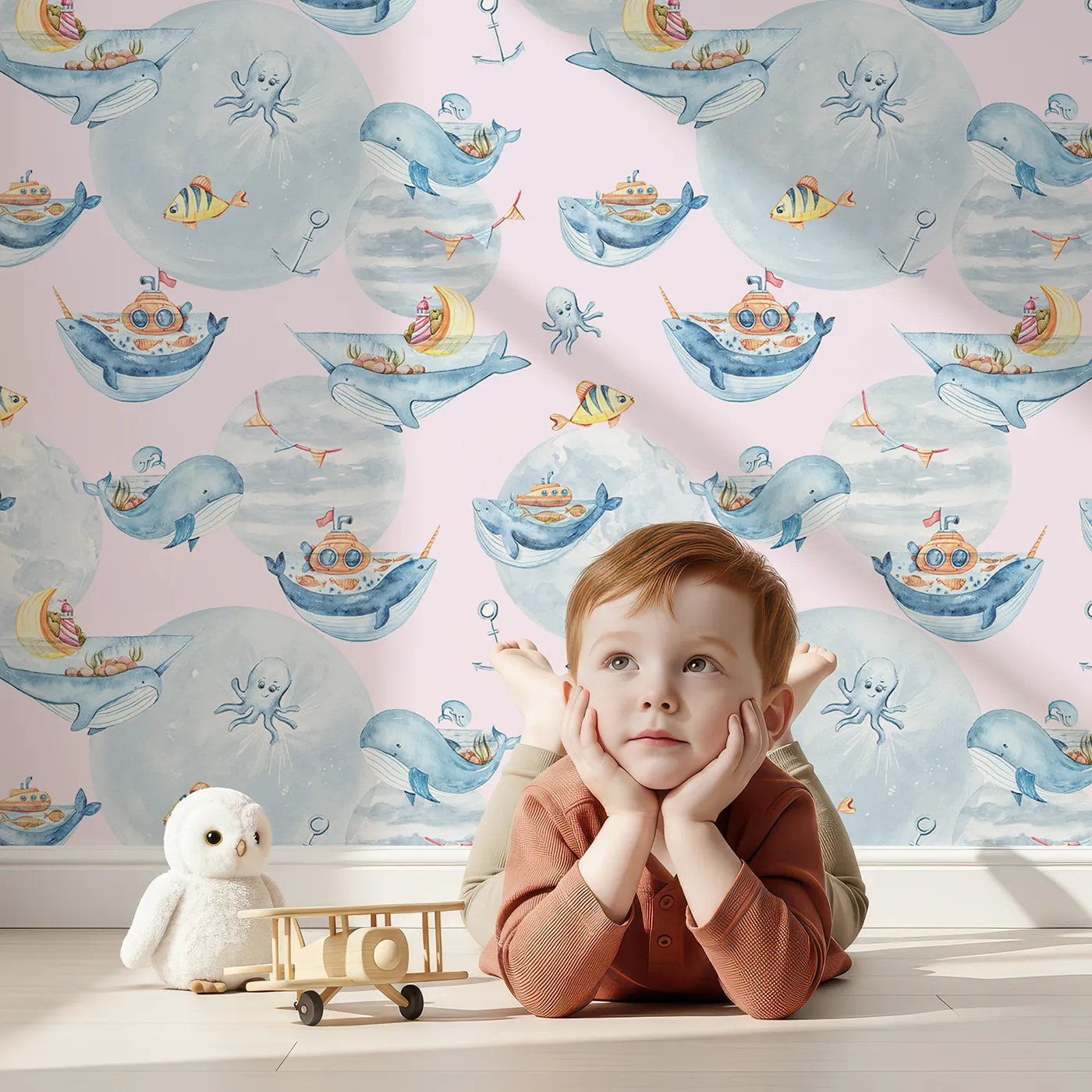 Lovely child standing in front of Whimsy Tots Whale Boat Parade Wallpaper in Pink with whale, submarine, boat, octopus, anchor, flag in design.