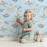 Lovely child standing in front of Whimsy Tots Whale Boat Parade Wallpaper in Blue with whale, submarine, boat, octopus, anchor, flag in design. Lovely child standing in front of Whimsy Tots Whale Boat Parade Wallpaper in Blue with whale, submarine, boat, octopus, anchor, flag in design.