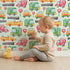 Lovely child standing in front of Whimsy Tots Little Car Parade Wallpaper in Mint Green with car, sign, road in design. Lovely child standing in front of Whimsy Tots Little Car Parade Wallpaper in Mint Green with car, sign, road in design.