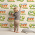 Lovely child standing in front of Whimsy Tots Cottage Garden Village Wallpaper in Cream with tree, bush, house in design. Lovely child standing in front of Whimsy Tots Cottage Garden Village Wallpaper in Cream with tree, bush, house in design.