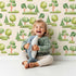 Lovely child standing in front of Whimsy Tots Forest Meadow Grove Wallpaper in Cream with tree, bush in design. Lovely child standing in front of Whimsy Tots Forest Meadow Grove Wallpaper in Cream with tree, bush in design.