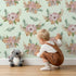 Lovely child standing in front of Whimsy Tots Rustic Blush Bouquet Wallpaper in Mint Green with flower, palm, leaf in design. Lovely child standing in front of Whimsy Tots Rustic Blush Bouquet Wallpaper in Mint Green with flower, palm, leaf in design.