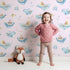 Lovely child standing in front of Whimsy Tots Whale Submarine Adventure Wallpaper in Blush Pink with whale, submarine, fish, anchor, octopus, bunting in design. Lovely child standing in front of Whimsy Tots Whale Submarine Adventure Wallpaper in Blush Pink with whale, submarine, fish, anchor, octopus, bunting in design.