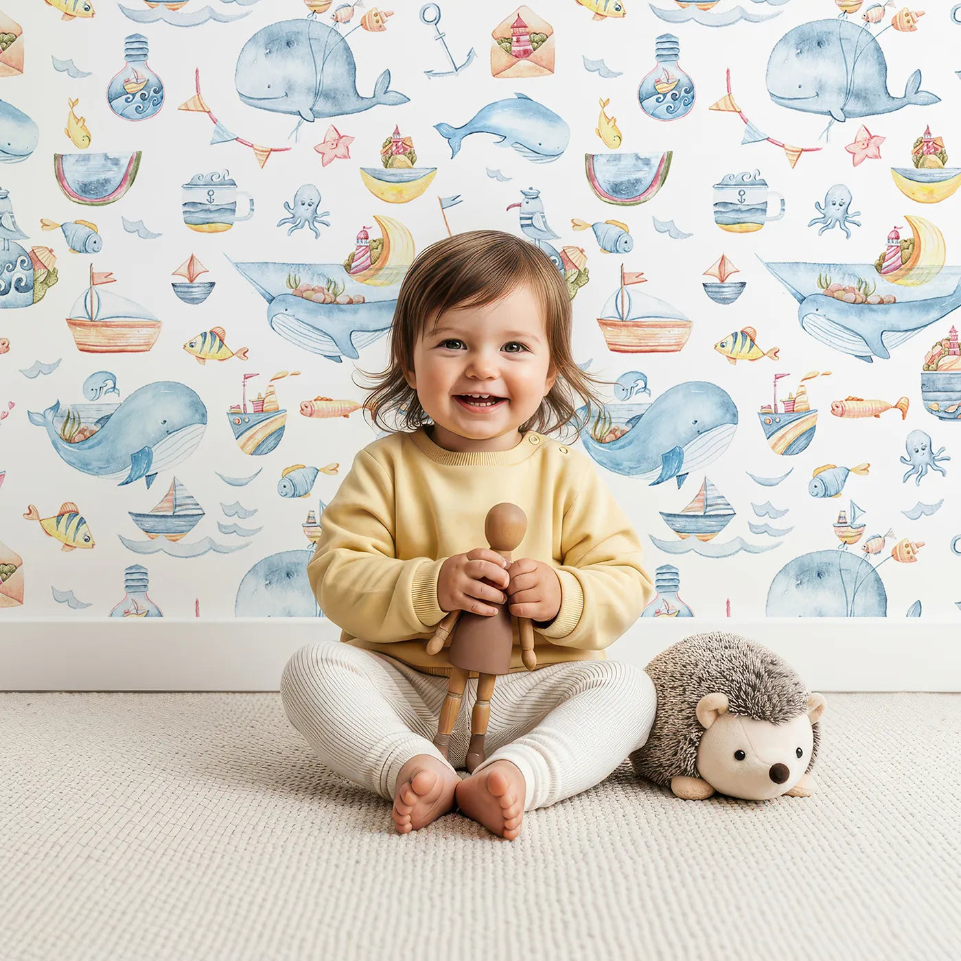 Lovely child standing in front of Whimsy Tots Whale Mail Wallpaper in White with whale, fish, octopus, boat, lighthouse, anchor, bird, mug, watermelon, letter in design.