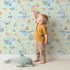 Lovely child standing in front of Whimsy Tots Whale Mail Wallpaper in Mint Green with whale, fish, octopus, boat, lighthouse, anchor, bird, mug, watermelon, letter in design. Lovely child standing in front of Whimsy Tots Whale Mail Wallpaper in Mint Green with whale, fish, octopus, boat, lighthouse, anchor, bird, mug, watermelon, letter in design.