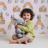 Lovely child standing in front of Whimsy Tots Rainbow Castle Dreams Wallpaper in Pink with castle, rainbow, moon, cloud, star, net in design. Lovely child standing in front of Whimsy Tots Rainbow Castle Dreams Wallpaper in Pink with castle, rainbow, moon, cloud, star, net in design.