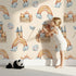 Lovely child standing in front of Whimsy Tots Rainbow Castle Dreams Wallpaper in Peach with castle, rainbow, moon, cloud, star, net in design. Lovely child standing in front of Whimsy Tots Rainbow Castle Dreams Wallpaper in Peach with castle, rainbow, moon, cloud, star, net in design.