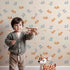 Lovely child standing in front of Whimsy Tots Wooden Star Sprinkle Wallpaper in Beige with star in design. Lovely child standing in front of Whimsy Tots Wooden Star Sprinkle Wallpaper in Beige with star in design.
