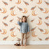 Lovely child standing in front of Whimsy Tots Moon Perch Birds Wallpaper in Beige with bird, moon in design. Lovely child standing in front of Whimsy Tots Moon Perch Birds Wallpaper in Beige with bird, moon in design.