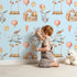 Lovely child standing in front of Whimsy Tots Dreamland Friends Wallpaper in Blue with bird, bunny, cloud, balloon, star in design. Lovely child standing in front of Whimsy Tots Dreamland Friends Wallpaper in Blue with bird, bunny, cloud, balloon, star in design.