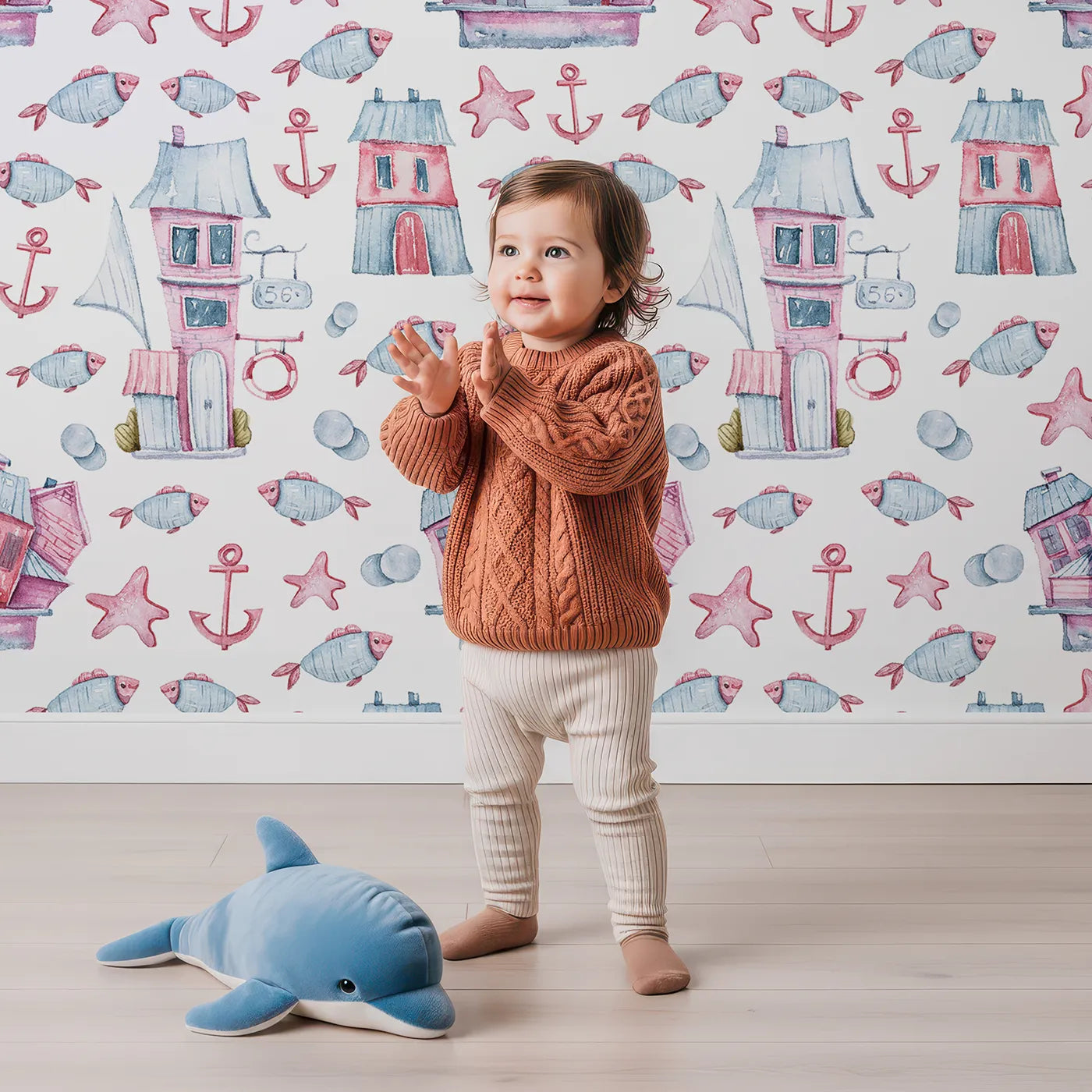 Lovely child standing in front of Whimsy Tots Seaside Village Parade Wallpaper in White with fish, house, anchor, starfish, bubble in design.