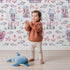 Lovely child standing in front of Whimsy Tots Seaside Village Parade Wallpaper in White with fish, house, anchor, starfish, bubble in design. Lovely child standing in front of Whimsy Tots Seaside Village Parade Wallpaper in White with fish, house, anchor, starfish, bubble in design.